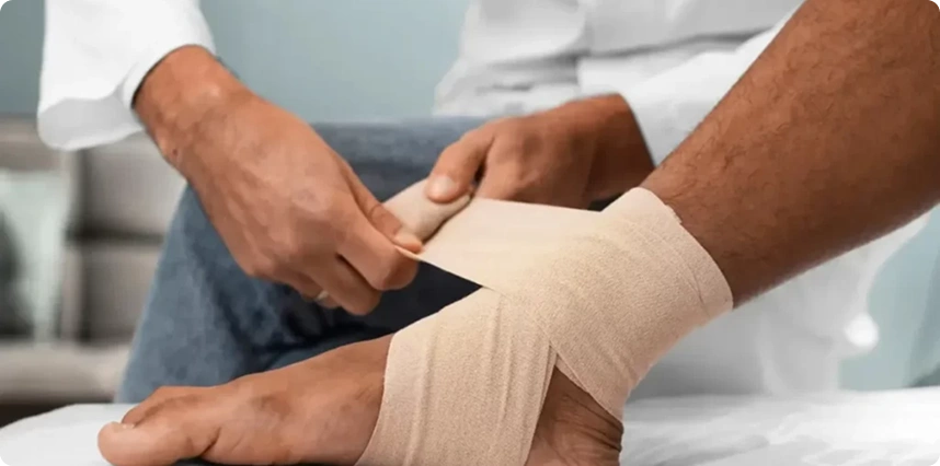 Doctor applying compression bandage to patient’s ankle injury.