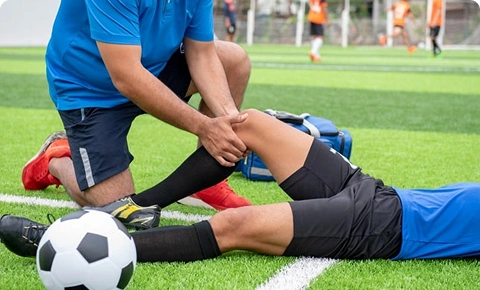 Sports physiotherapist examining a football player’s knee injury on the field.
